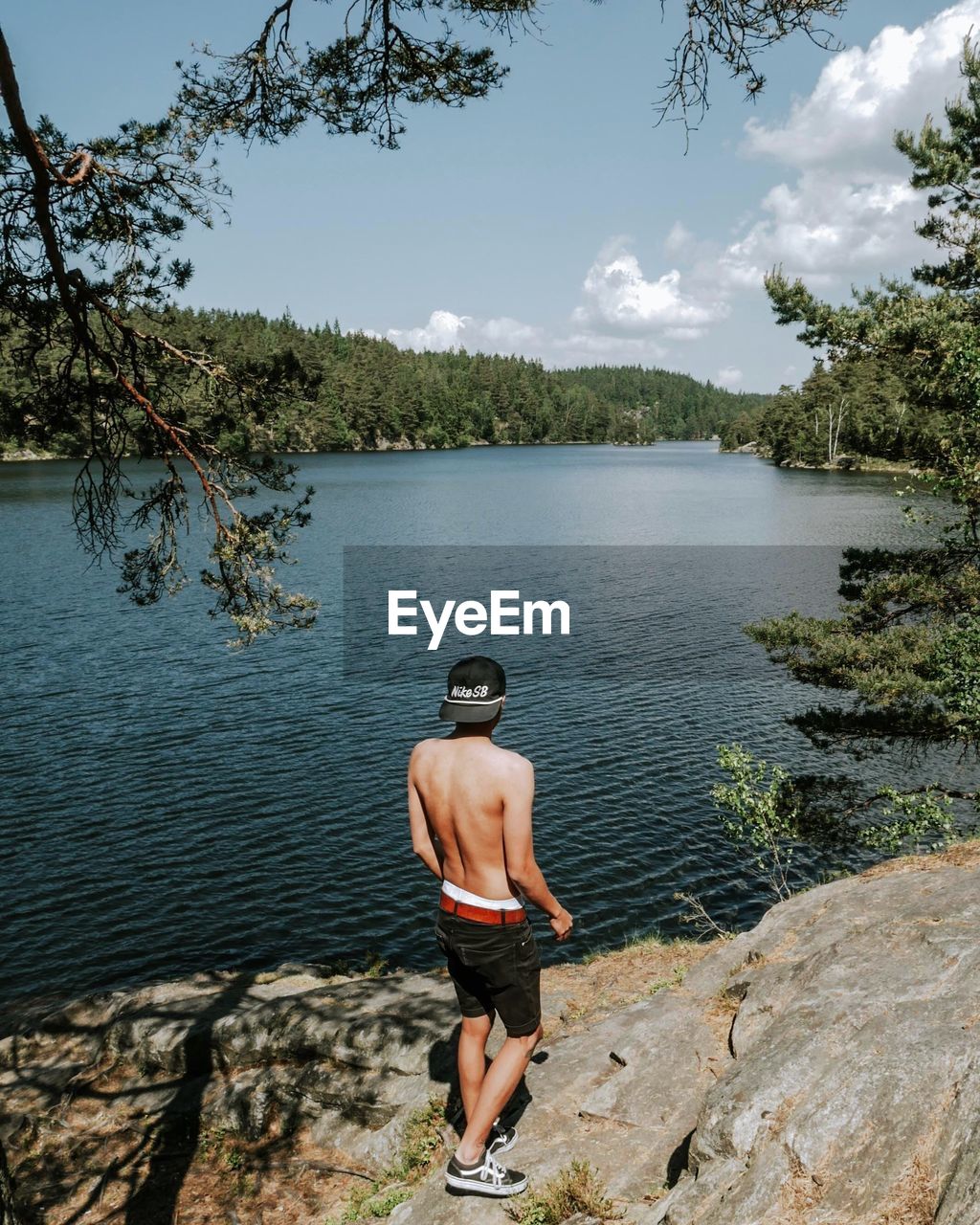 REAR VIEW OF SHIRTLESS MAN STANDING ON ROCK