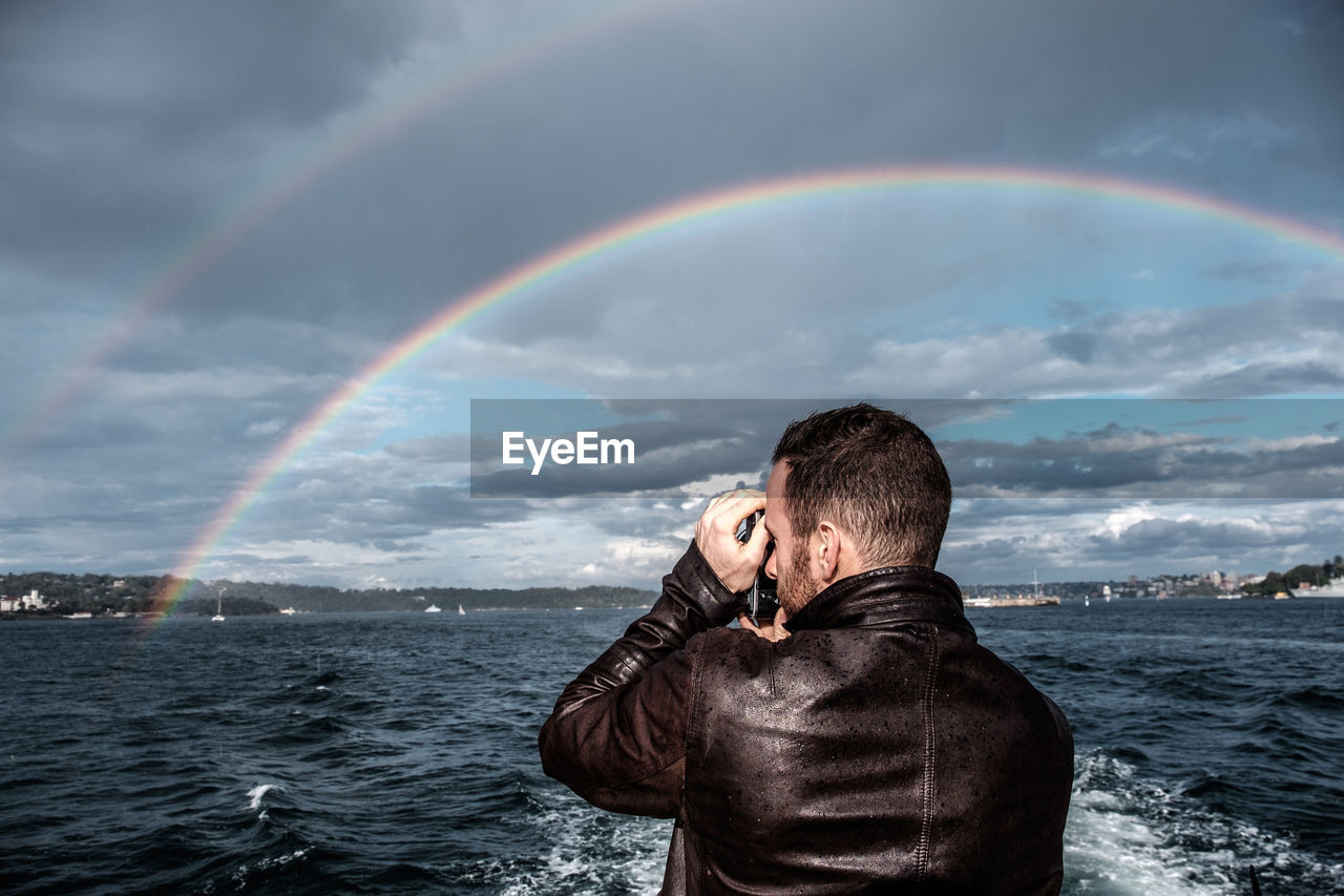 Scenic view of man taking photograph of  rainbow in front of sea against sky