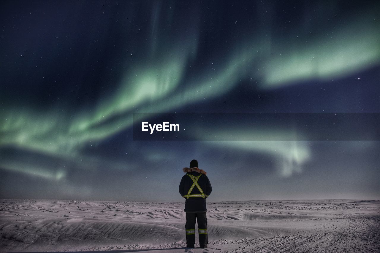 Man looking at northern light while standing on snowcapped landscape