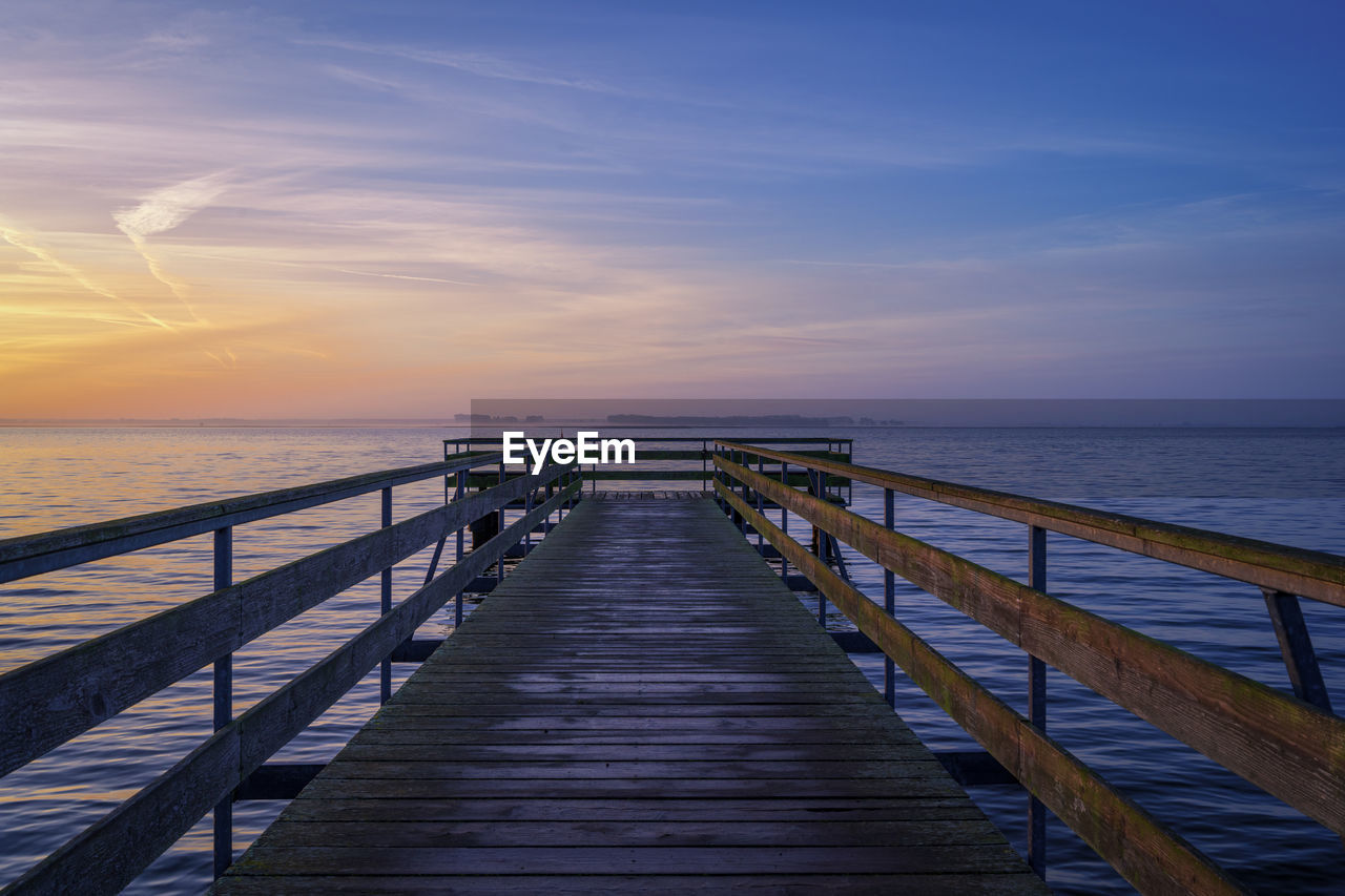 sky, water, sea, pier, horizon, horizon over water, ocean, scenics - nature, beauty in nature, sunset, nature, tranquility, walkway, the way forward, railing, coast, tranquil scene, wood, boardwalk, beach, shore, land, cloud, architecture, idyllic, reflection, no people, jetty, dusk, blue, diminishing perspective, evening, sunlight, built structure, outdoors, non-urban scene, footpath, seascape, bridge, travel destinations, footbridge, travel, wave, vanishing point, holiday, transportation, dock