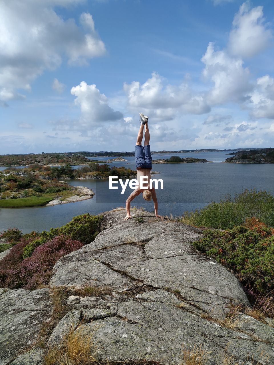 Man standing on rock by sea against sky