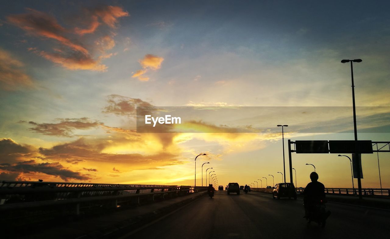 Vehicles on highway against sky at sunset