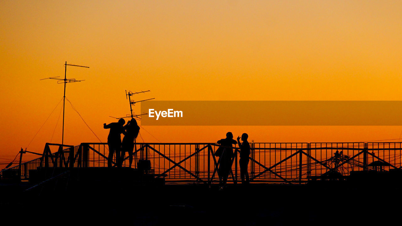 SILHOUETTE MAN AND WOMAN STANDING ON SEA AGAINST ORANGE SKY