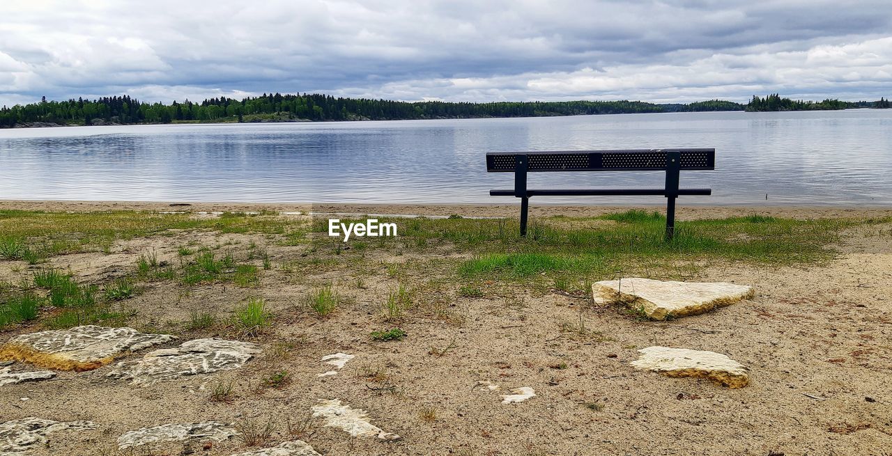 EMPTY BENCH AT LAKE AGAINST SKY