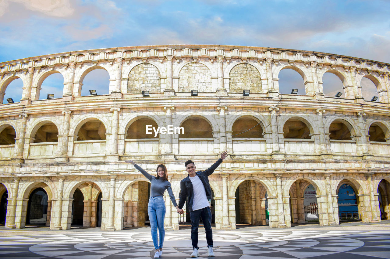 Portrait of couple holding hands while standing against historic building