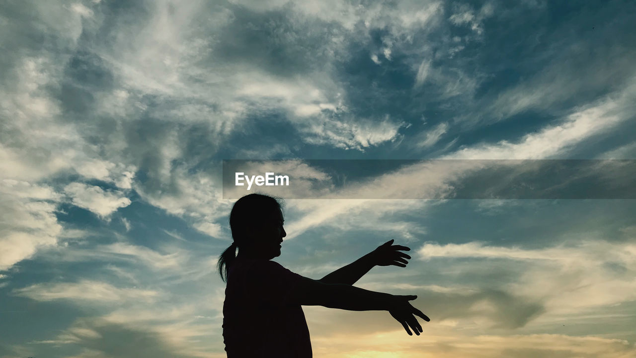 Silhouette woman standing against cloudy sky