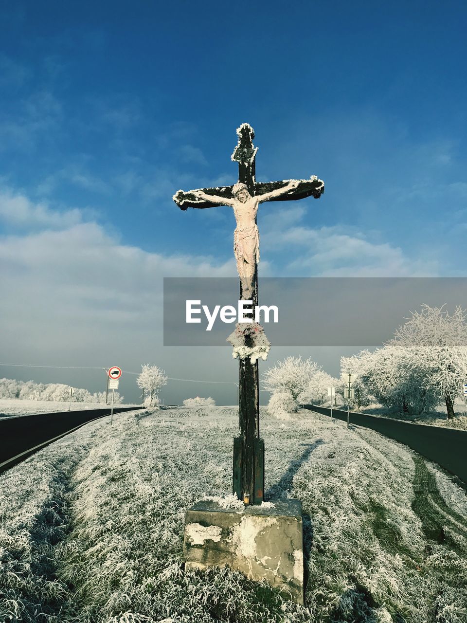 Statue on cross against sky during winter