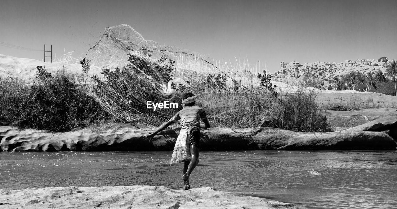 Rear view of fisherman throwing fishing net in lake