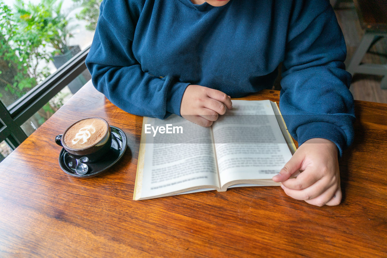 Midsection of man reading book on table