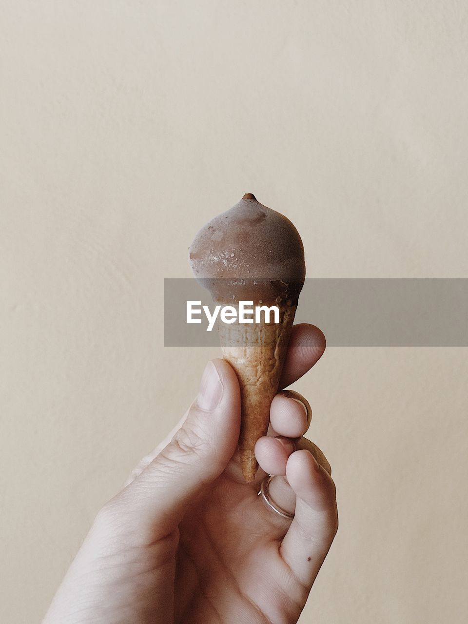 Cropped hand having ice cream cone against brown wall