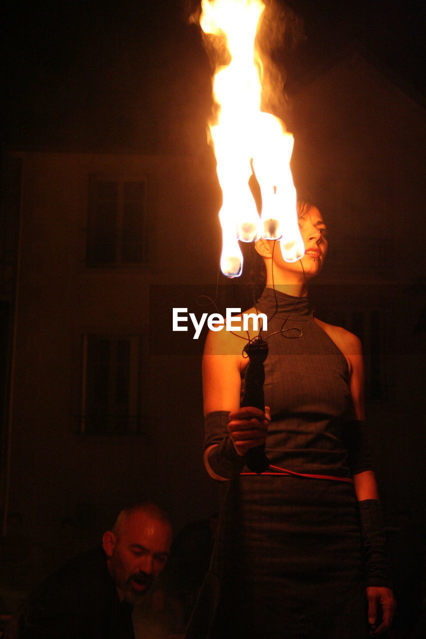 REAR VIEW OF WOMAN STANDING BY ILLUMINATED FIRE