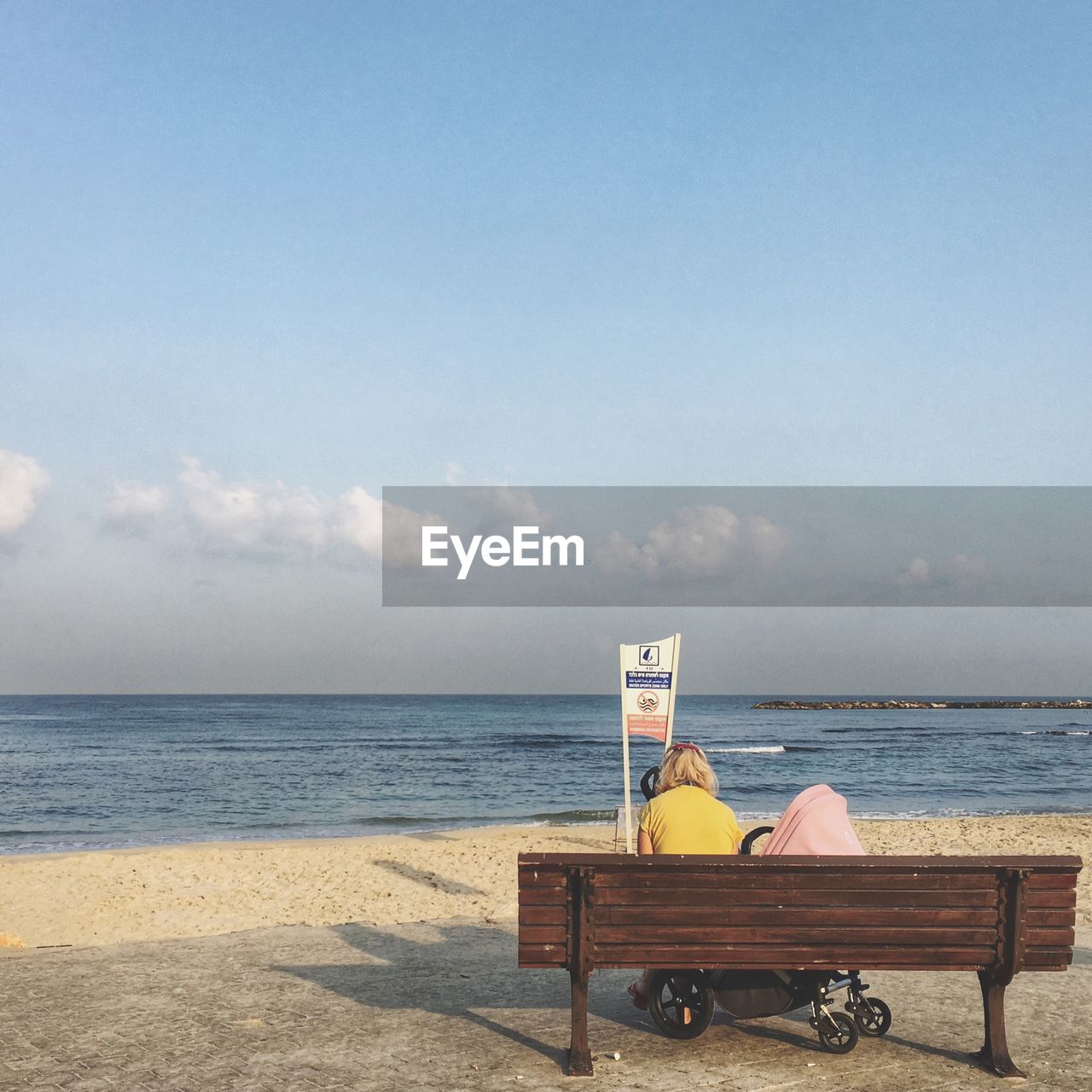 People sitting on bench at beach against sky