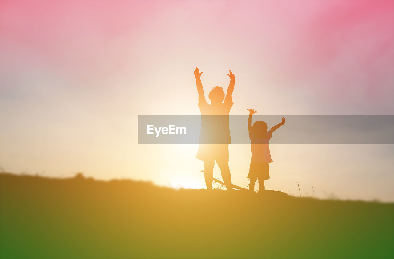 Low angle view of friends standing on field against sky during sunset