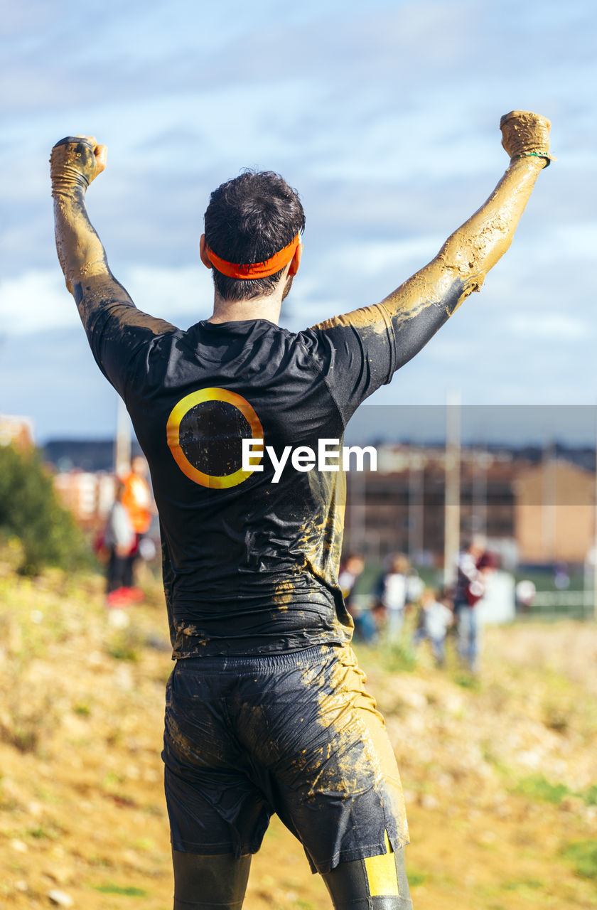 Participant in extreme obstacle race cheering, rear view