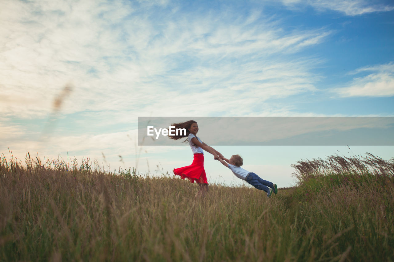 Girl carrying brother on field against sky