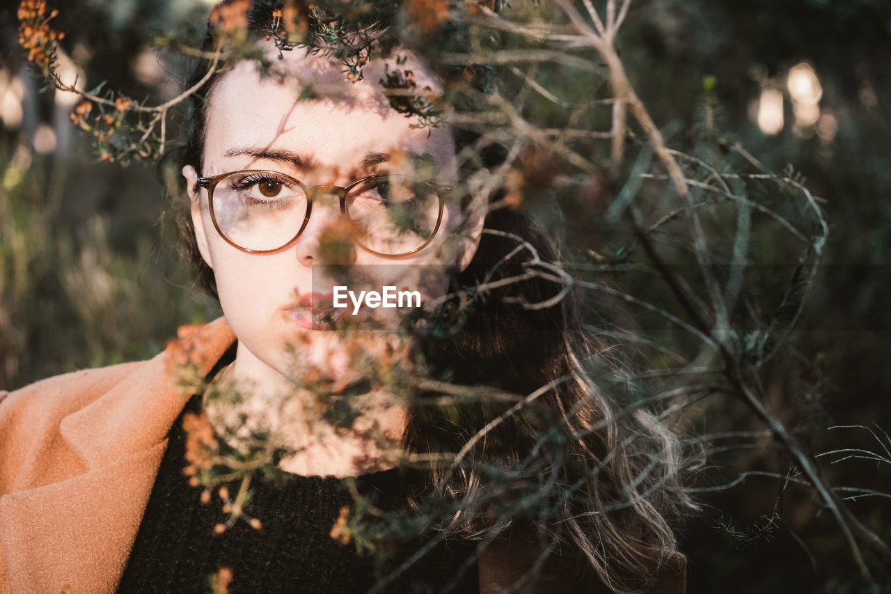 Close-up portrait of young woman wearing eyeglasses by plants in park