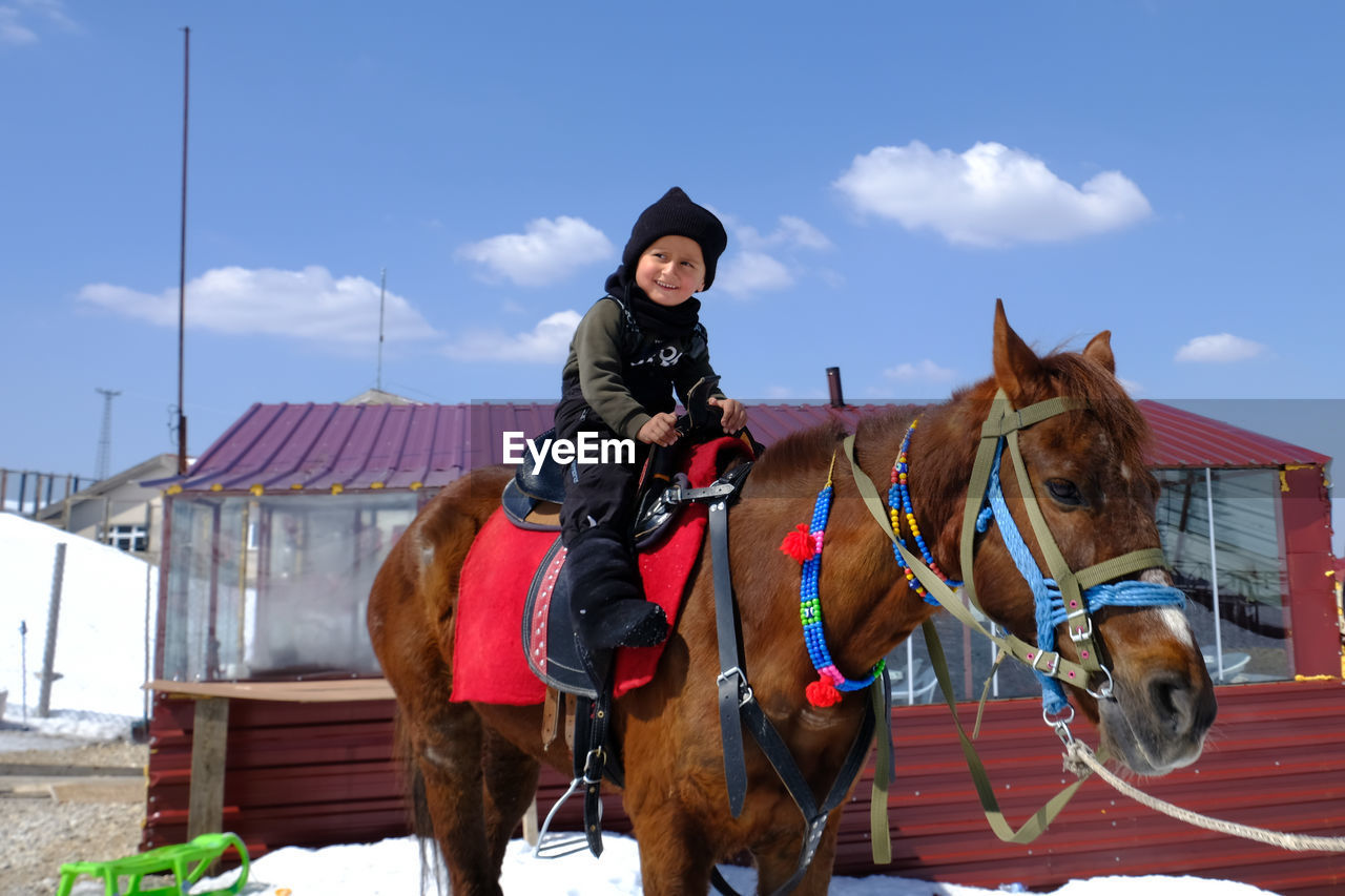 Rear view of child riding horse against sky