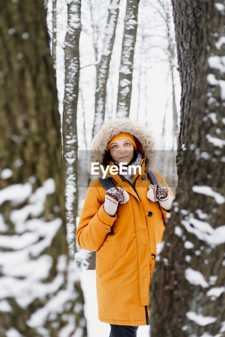 PORTRAIT OF WOMAN STANDING AGAINST SNOW COVERED TREE