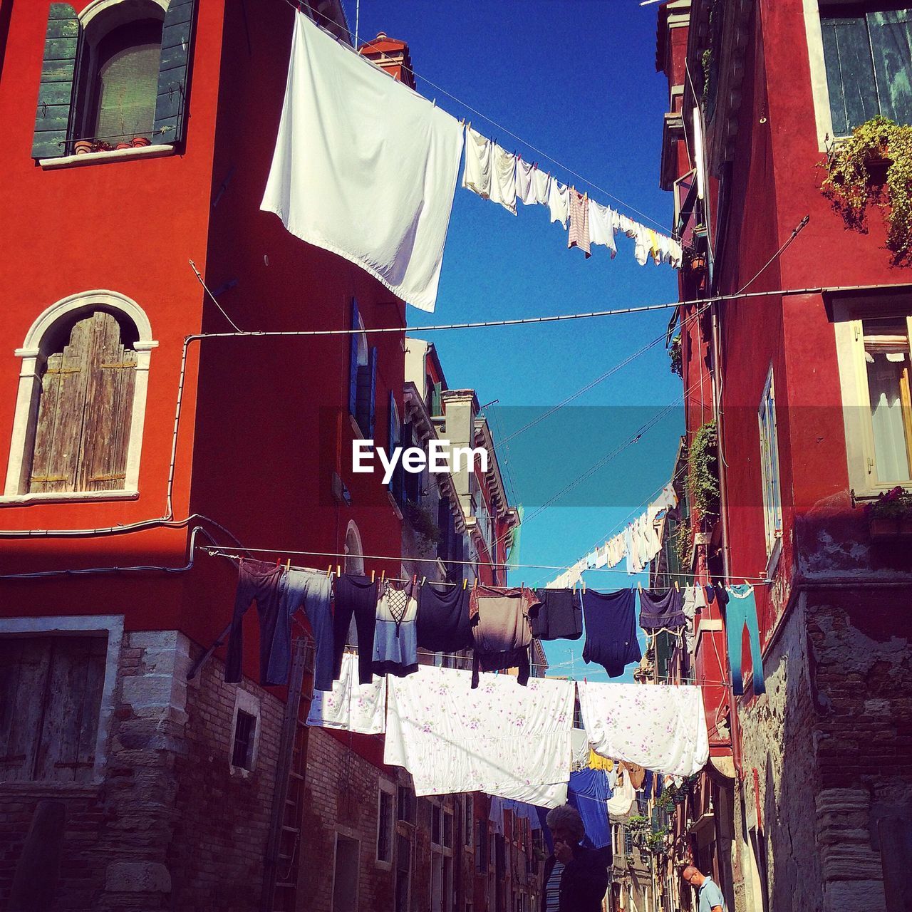 Low angle view of clothes lines between buildings against blue sky