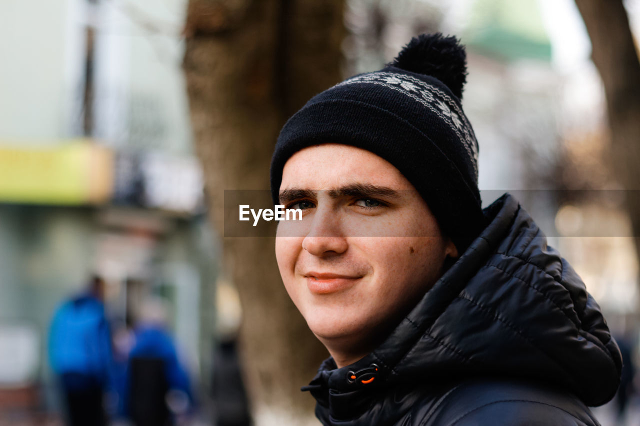 Close-up portrait of young man in warm hat outside on city urban background. happy millennial 