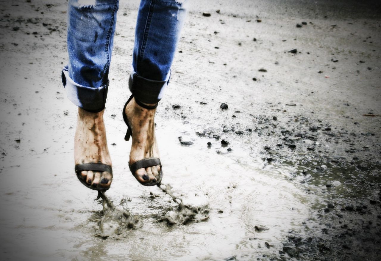 Low section of woman jumping over mud during monsoon