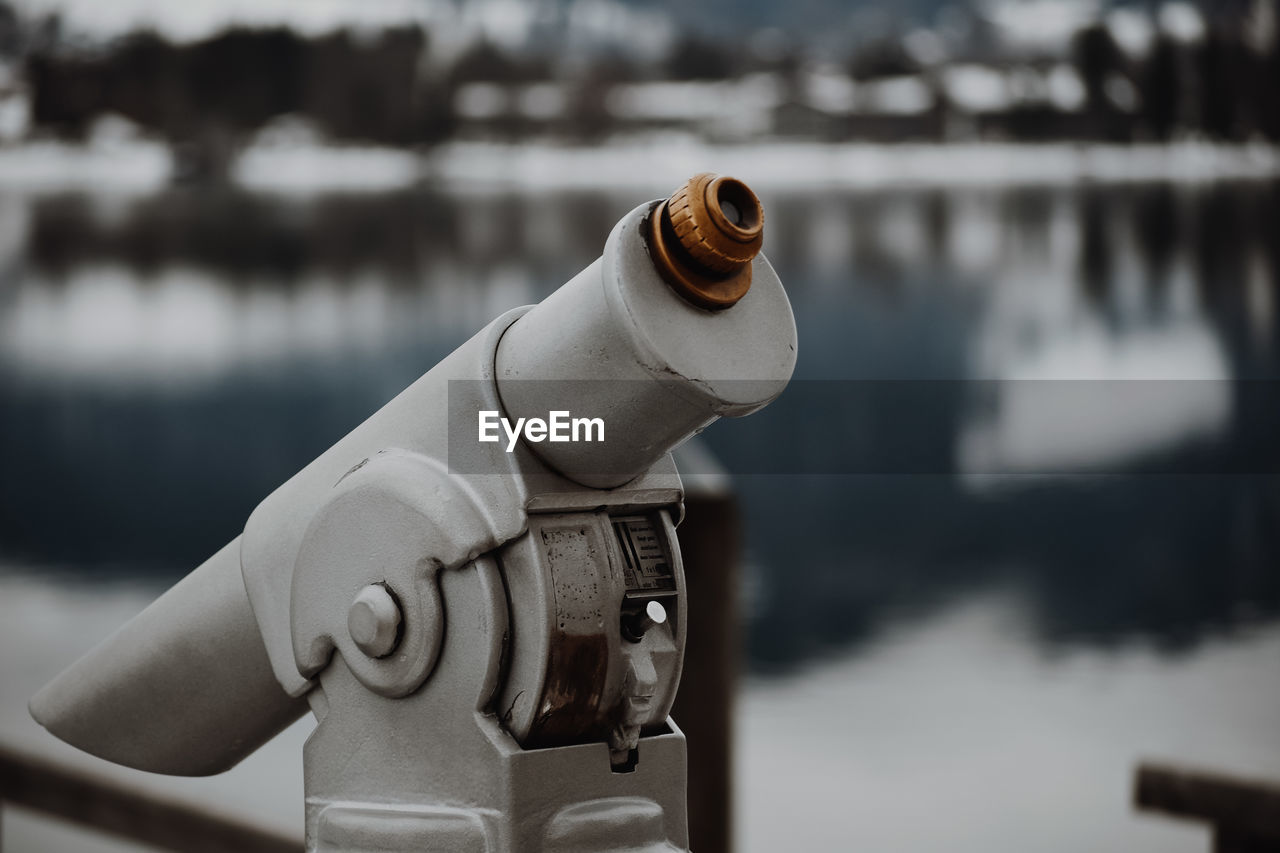 CLOSE-UP OF COIN-OPERATED BINOCULARS BY LAKE AGAINST BLURRED BACKGROUND