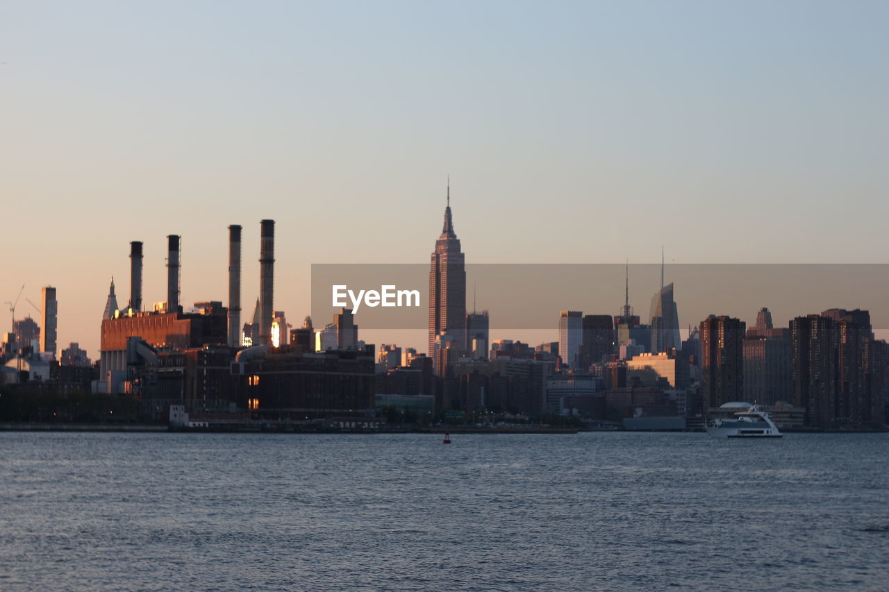 Empire state building and east river against clear sky during sunset in city