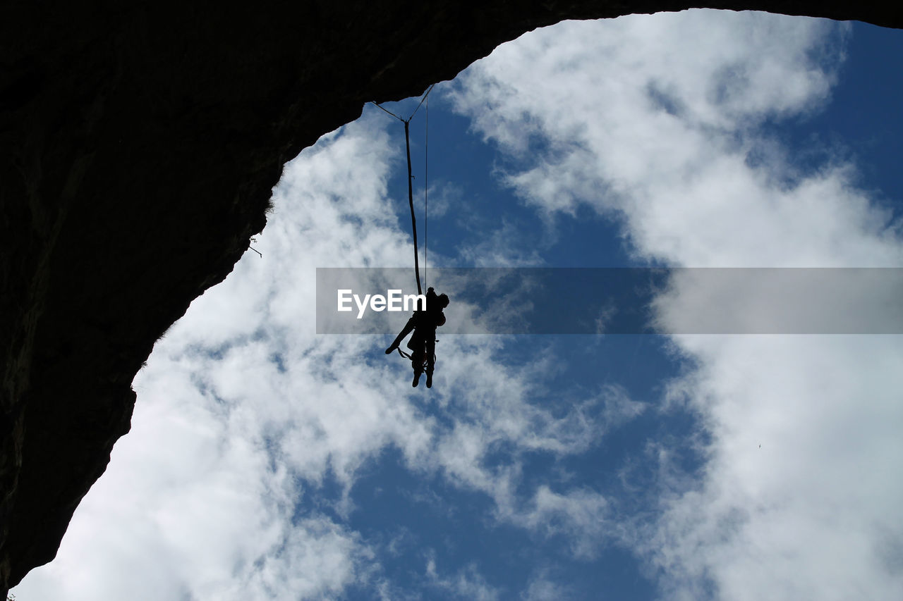 Low angle view of silhouette people climbing on cliff against sky