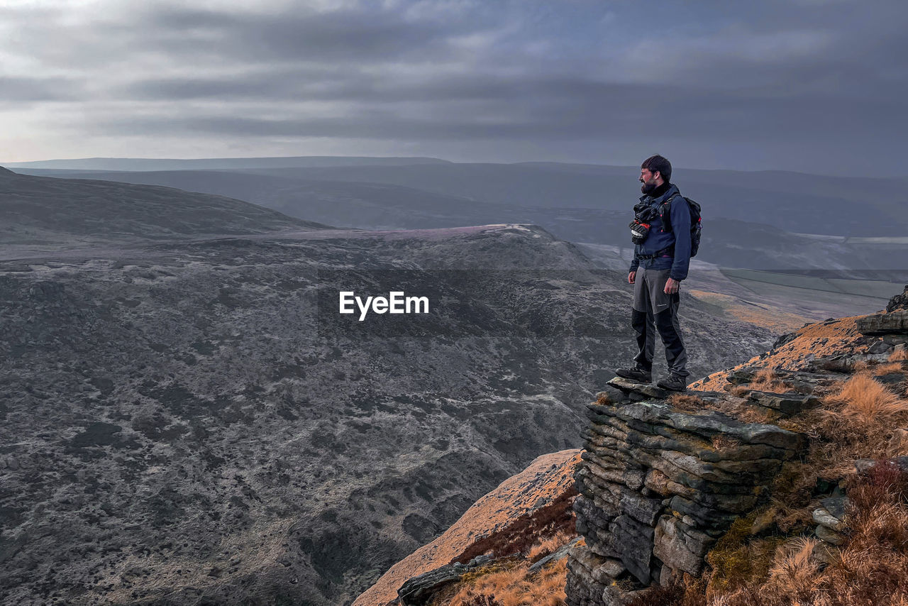 Lone hiker standing on cliff edge in the mountains overlooking the hills 