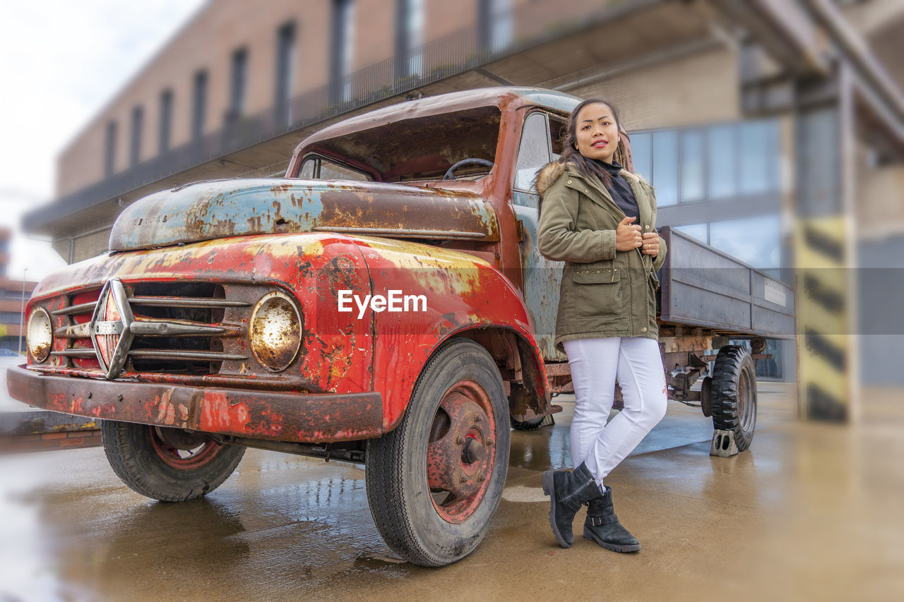 Portrait of woman standing on floor by old car
