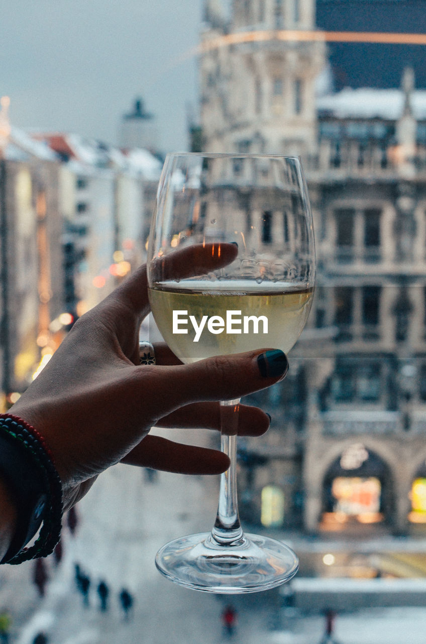 Close-up of hand holding wineglass against city