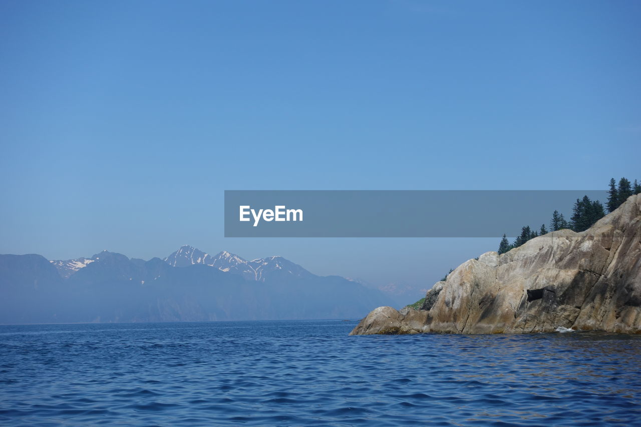 Scenic view of sea and mountains against clear blue sky