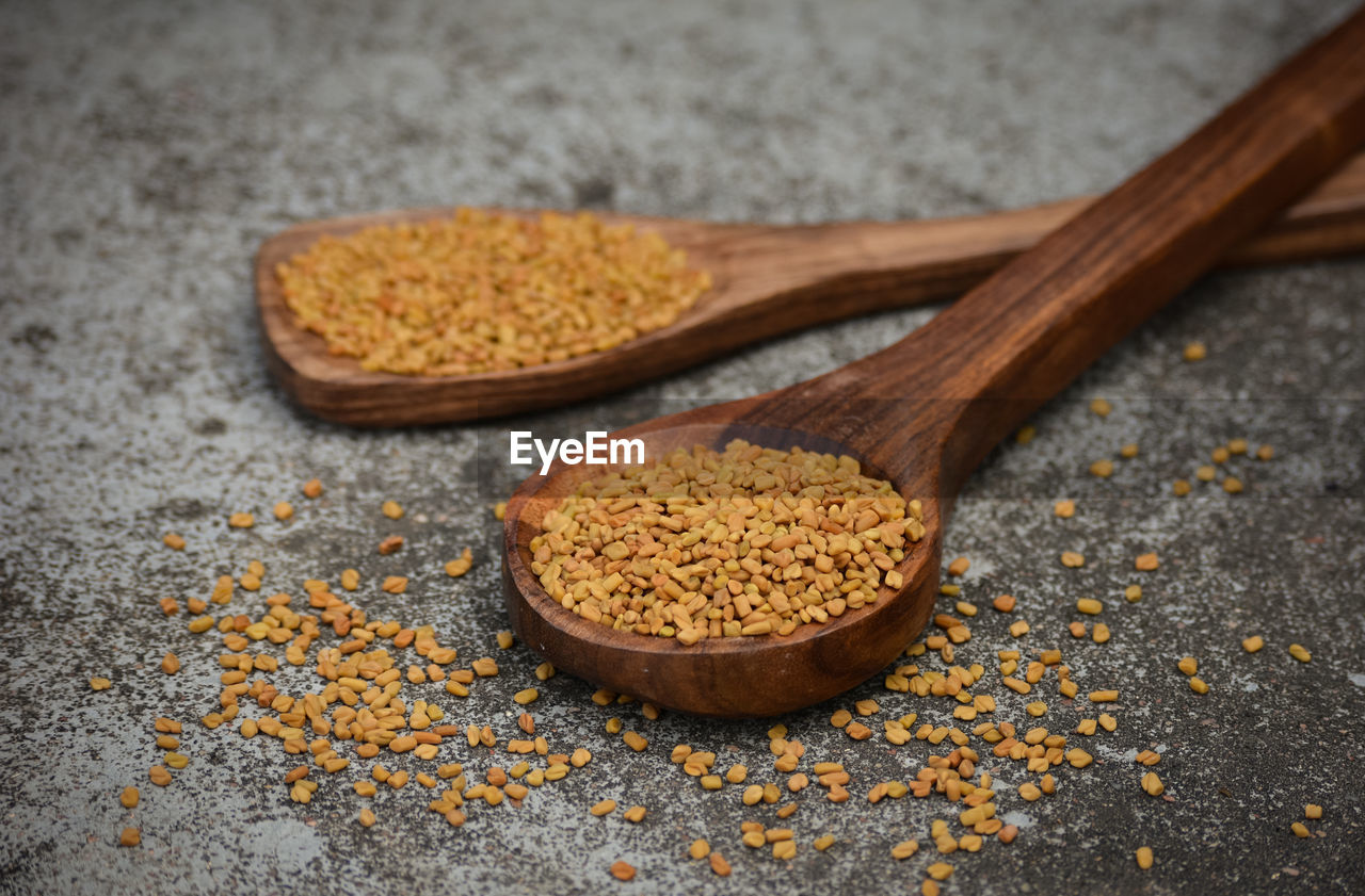 Fenugreek seeds in wooden spoon on textured background
