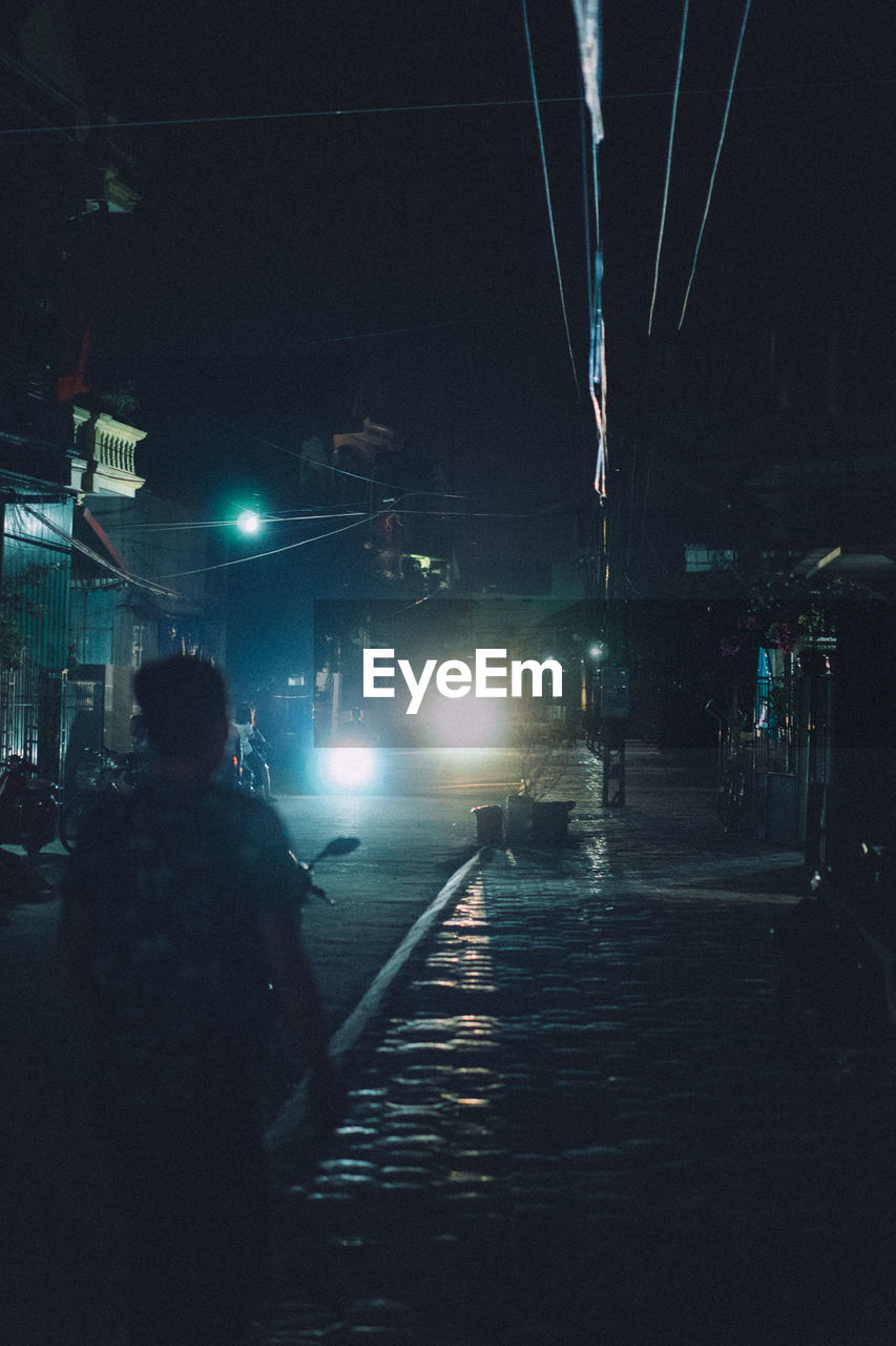 MAN WALKING ON ILLUMINATED STREET AT NIGHT