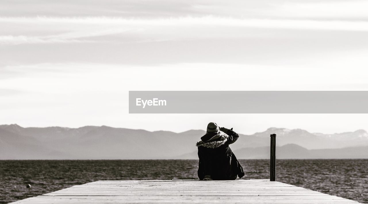 Rear view of person sitting on pier over lake