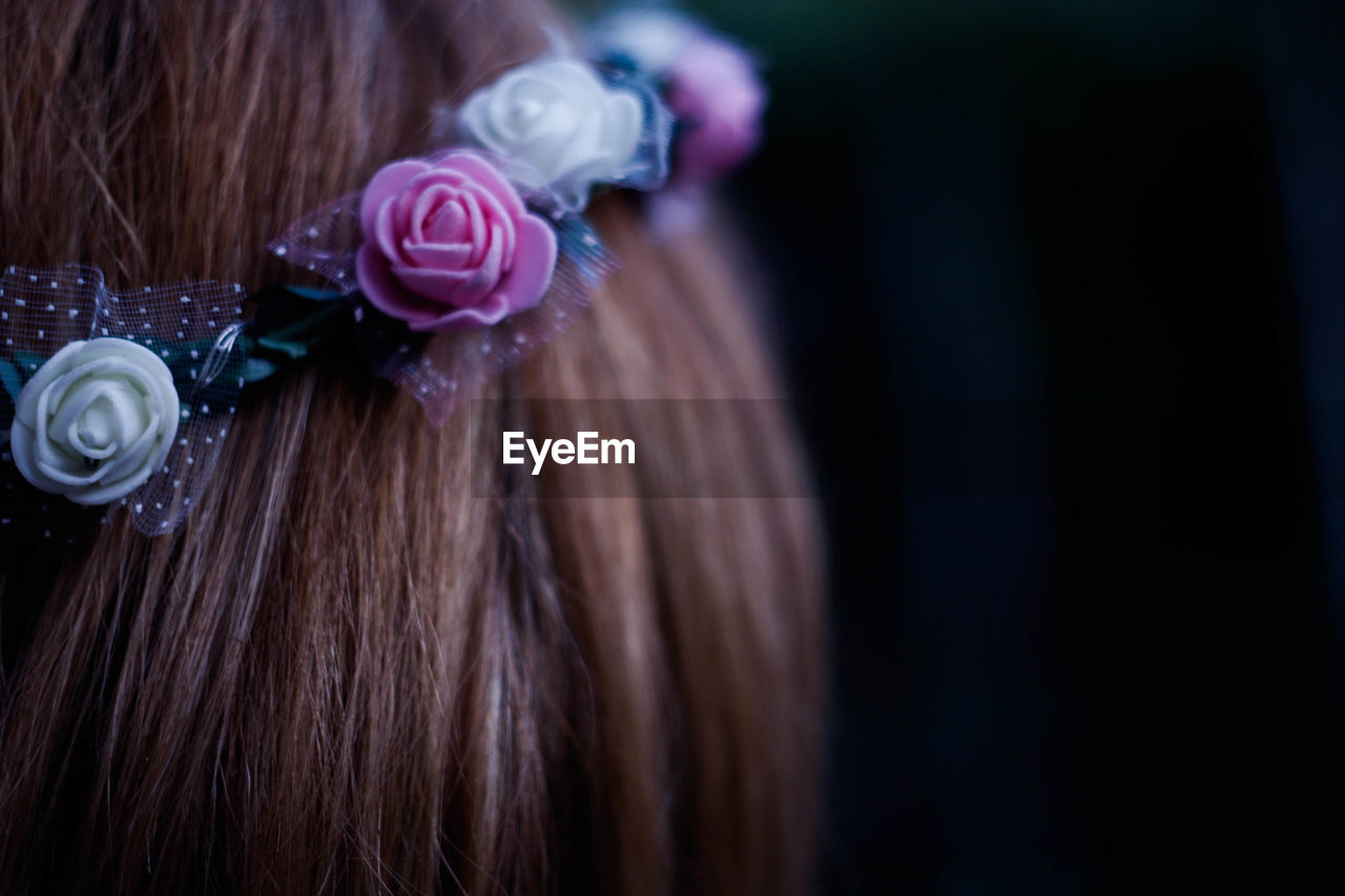 Close-up of woman wearing flowers on hair against black background