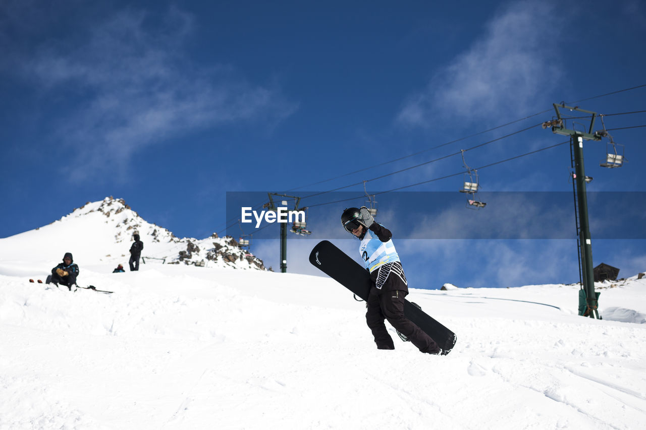 Man holding snowboard while standing on snow covered field against sky