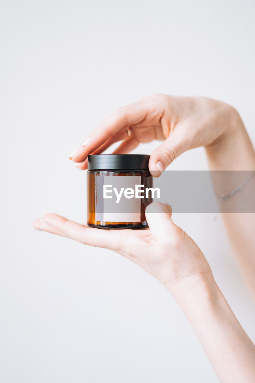 Women's hands hold glass jar with empty label on light background, mockup