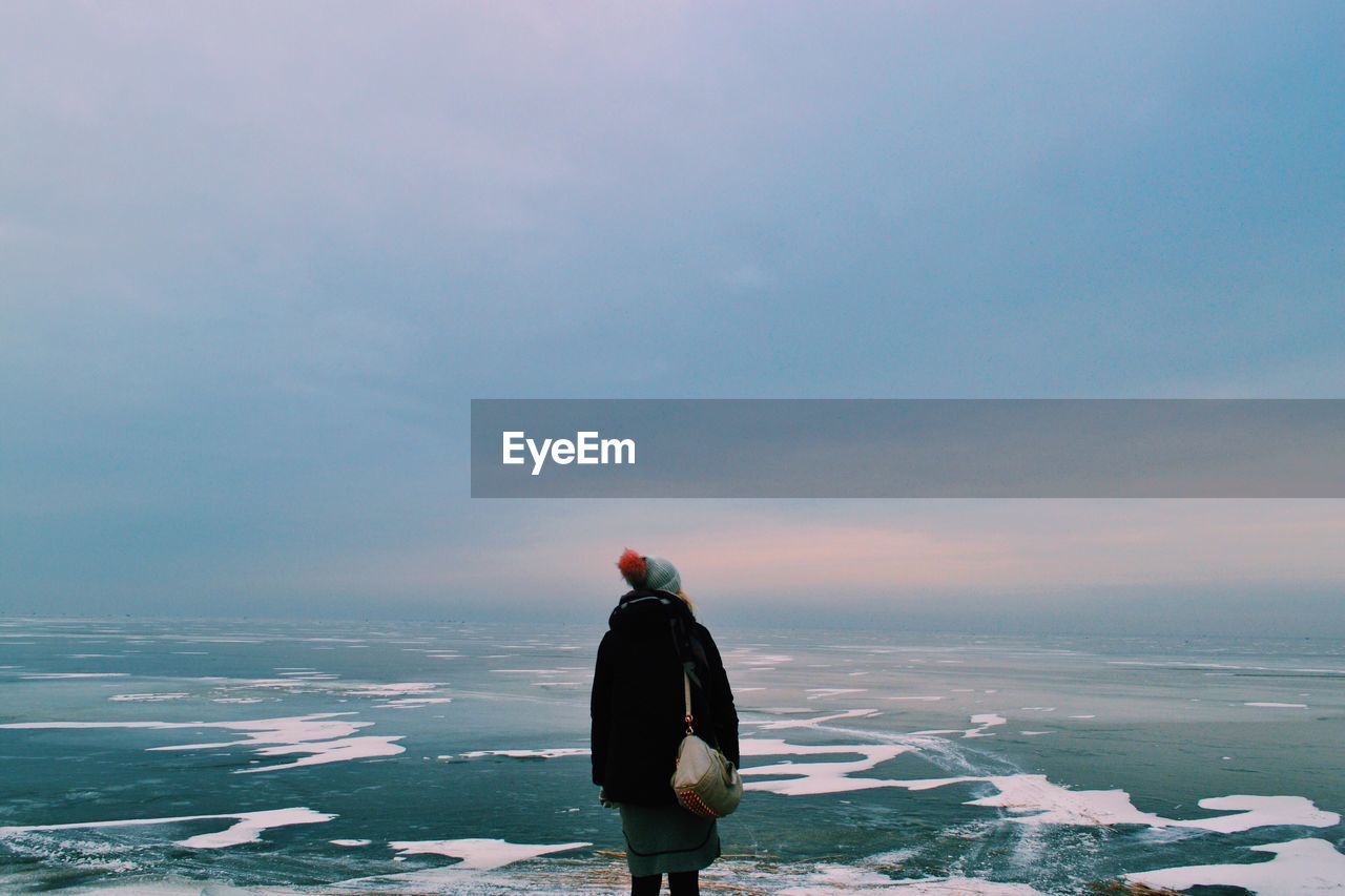 Rear view of woman looking at landscape against cloudy sky during winter