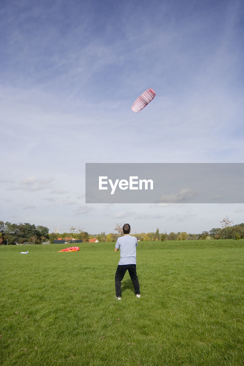 Rear view full length of man flying kite on grassy field against sky