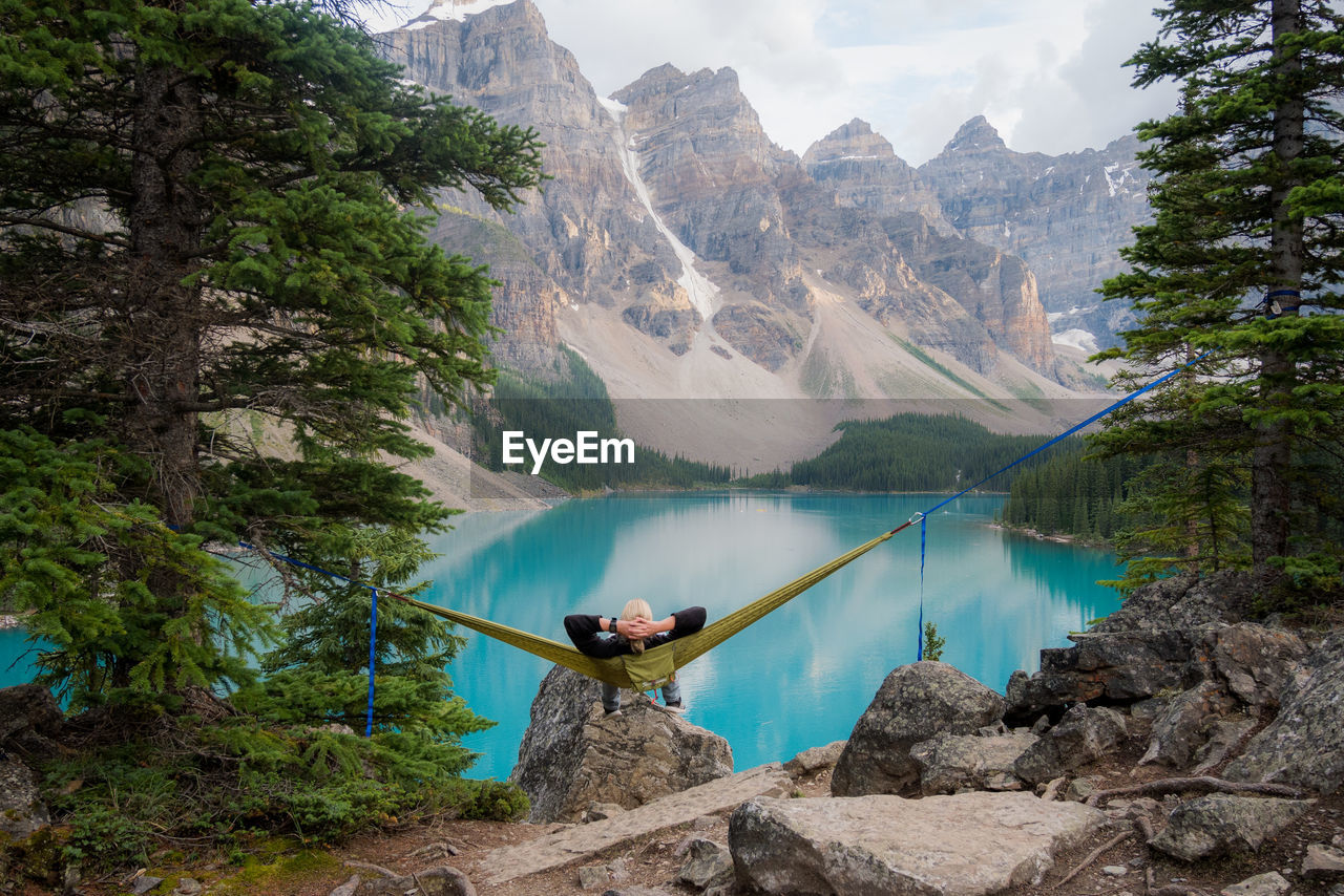 High angle rear view of man resting on hammock in front of lake in mountainous landscape