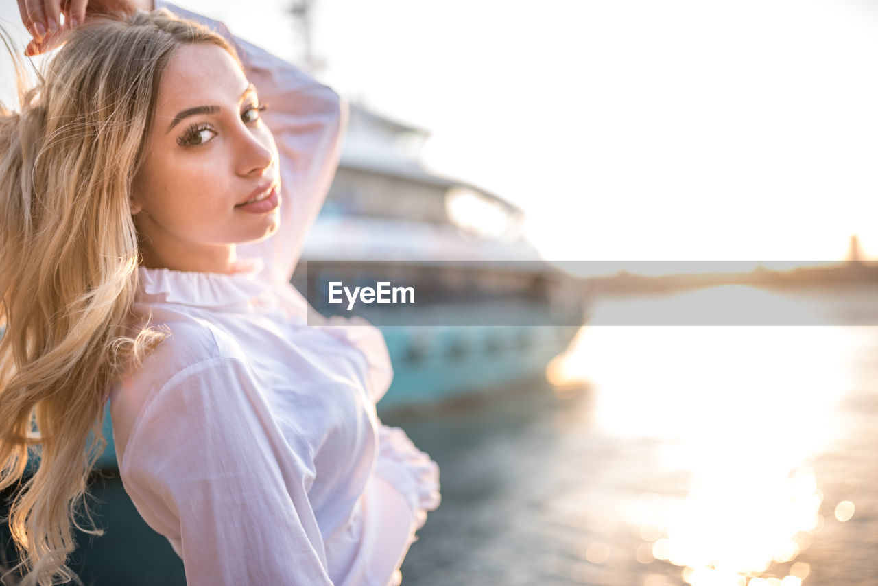 Portrait of beautiful woman standing against ship in river during sunset