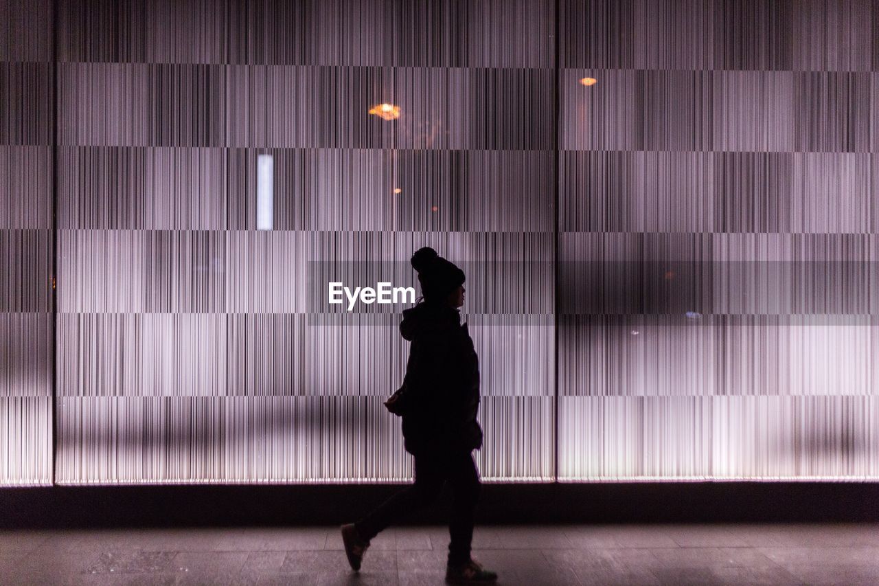 Side view of silhouette woman walking on footpath by patterned glass