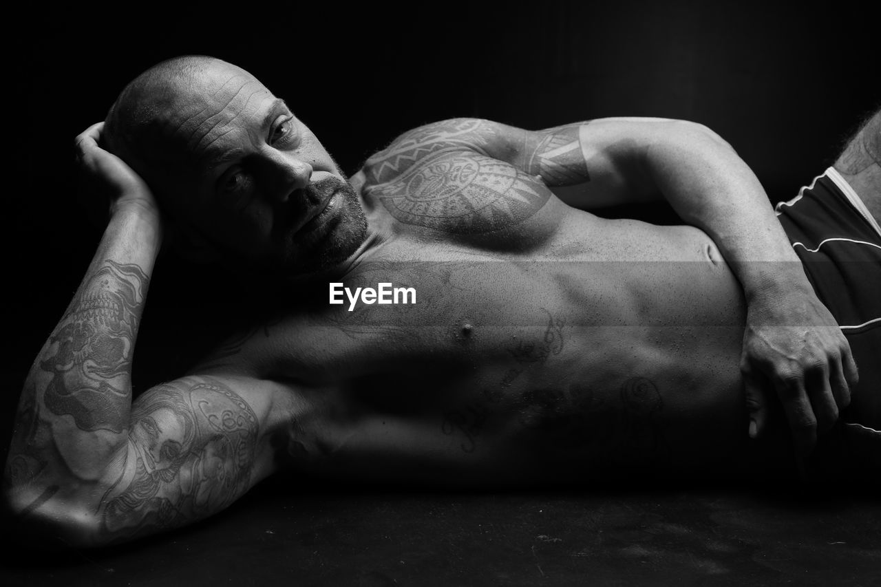 Portrait of shirtless man lying on black background