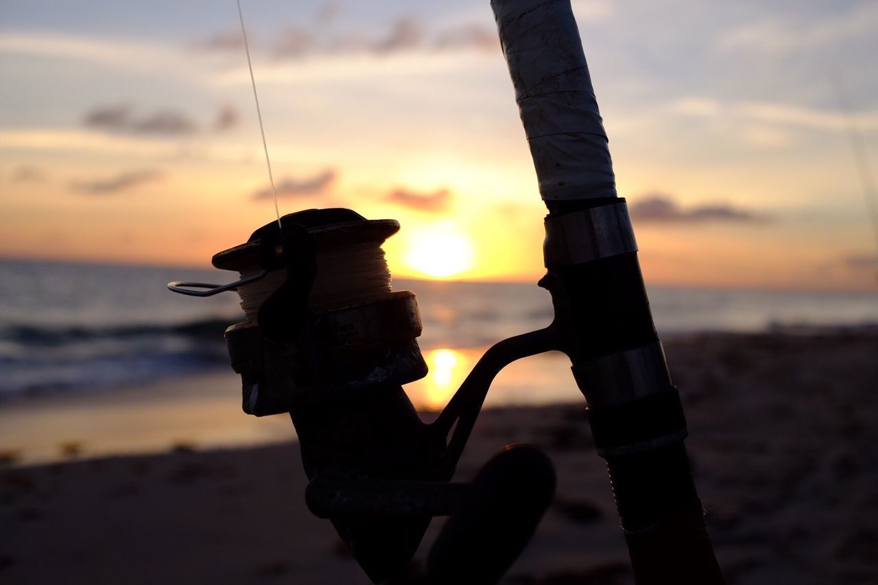 Close-up of fishing rod on shore at beach against sky during sunset