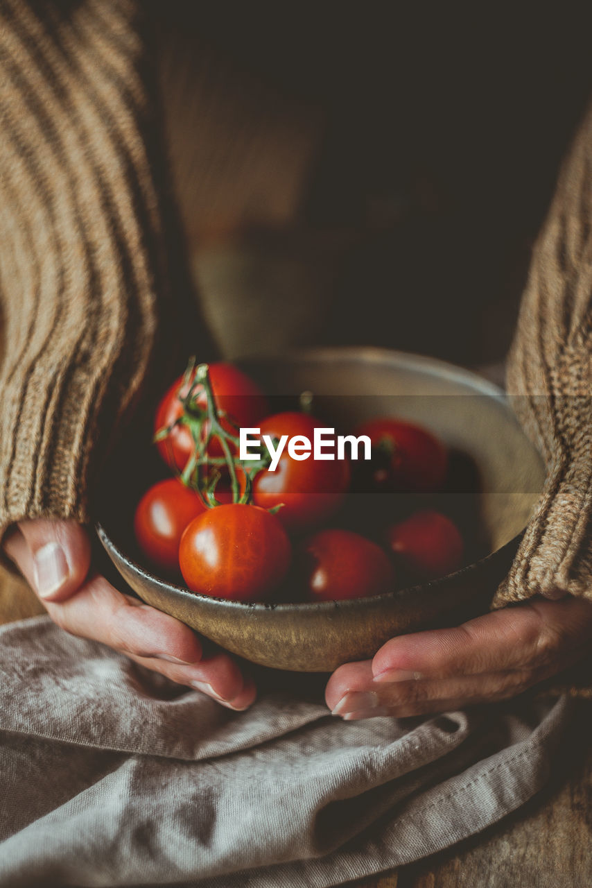 Cropped hands of woman holding bowl with cherry tomatoes on table