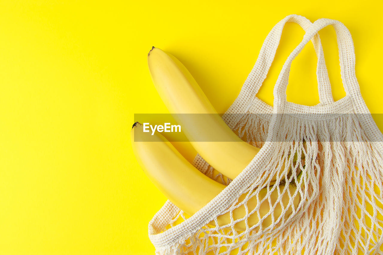Ripe bananas in a mesh bag on a yellow background. eco-friendly cotton shopping bag. organic fruits.