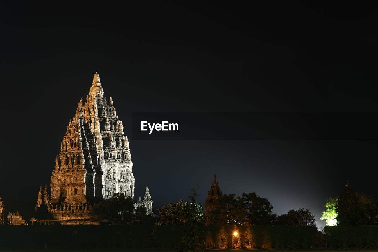 LOW ANGLE VIEW OF ILLUMINATED TEMPLE BUILDING AGAINST SKY AT NIGHT