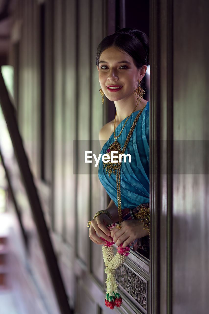 Women wearing thai national costumes standing by the window of a thai house