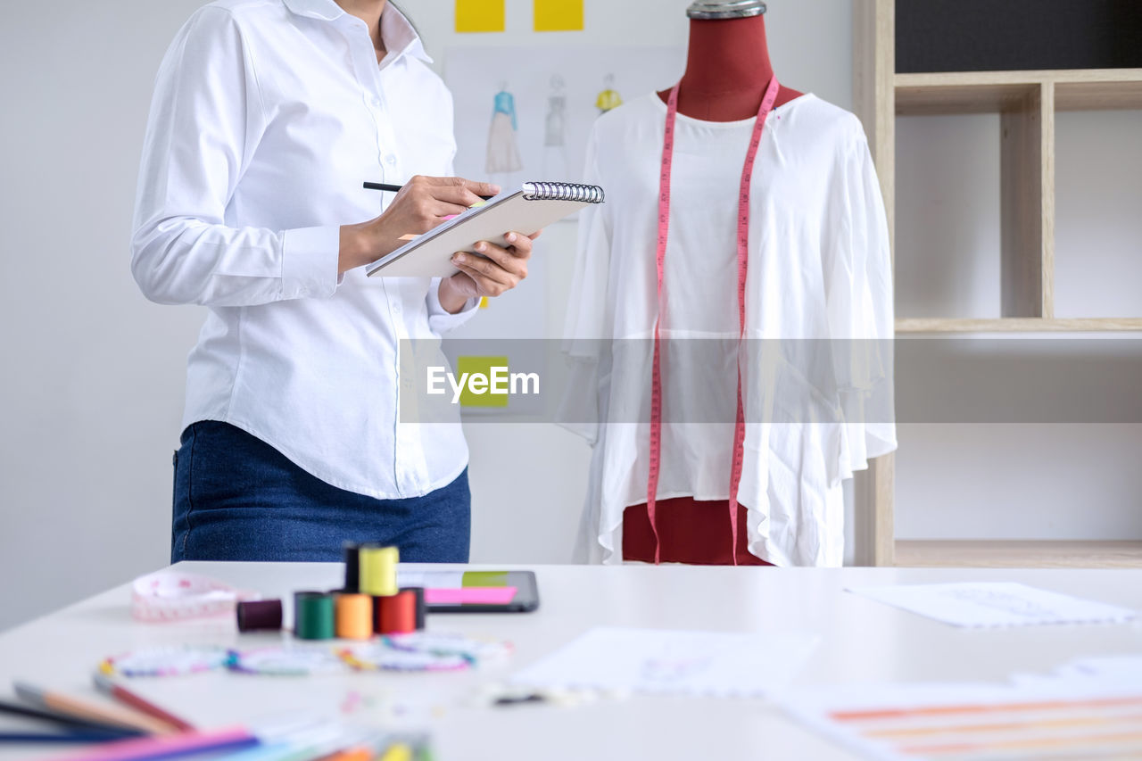 Midsection of female fashion designer drawing on book in office